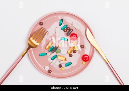 A plate full of capsules and tablets of different shapes and sizes with knife and fork, top view. Nutritional supplements, healthy eating concept Stock Photo
