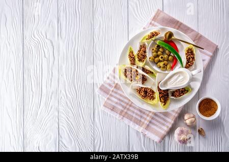 Spicy ground beef and chopped green olives Endive Boats served on a white plate with sour cream, olives, chili peppers, horizontal view from above, fl Stock Photo