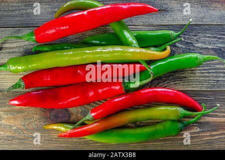 Mix of heap of raw red and green chili pappers or Capsicum frutescens,  on dark wooden table. Food background. Top view. Selective focus. Close-up. Stock Photo