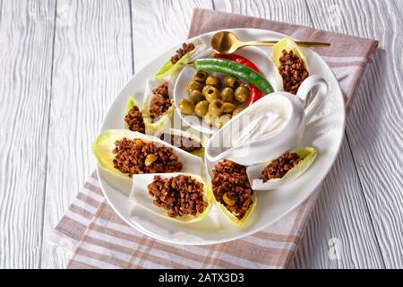 close-up of ground beef and chopped green olives Endive Boats served on a white plate with sour cream, olives, chili peppers Stock Photo