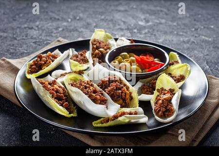 low-carb Ground Beef and chopped green olives Endive Boats served on a black plate on a grey concrete table, horizontal view from above Stock Photo