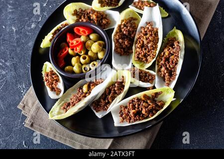 low-carb Ground Beef and chopped green olives Endive Boats served on a black plate on a grey concrete table, horizontal view from above, close-up Stock Photo