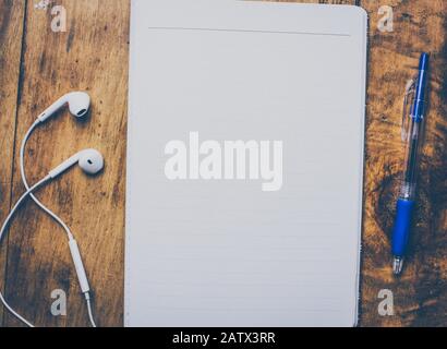 Blank notebook with pen are on top of wood office desk table. White earphones next to it. Top view, flat lay. retro effect. Vintage style Stock Photo
