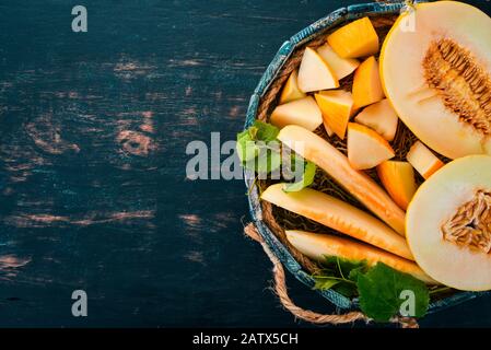 Melon in a wooden box. Sliced to pieces of melon. On a wooden background. Free space for text. Top view. Stock Photo