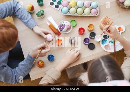 High angle view of two friends sitting together at the table and painting Easter eggs with paintbrushes Stock Photo