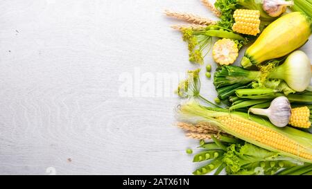 A large selection of raw fresh vegetables. Corn, zucchini, lettuce, greens. On a black wooden background. Top view. Free space for your text. Stock Photo