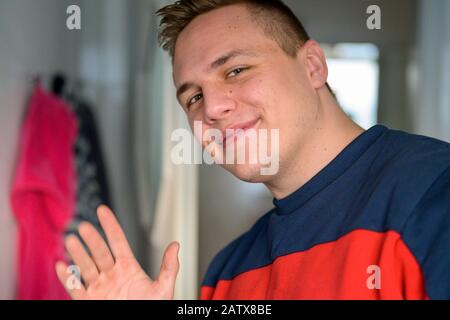 Happy cheerful attractive young man waving at the camera indoors in a bathroom in a close up cropped portrait Stock Photo
