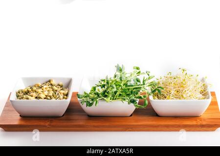 Fresh snow pea, mung and alfalfa sprouts in white bowls on wooden tray. Healthy diet superfood and micro green eating concept Stock Photo