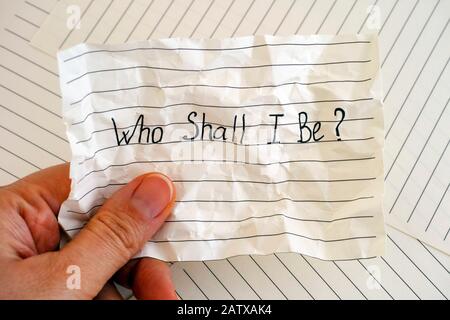 Woman hand holding crumpled lined paper with words Who Shall I Be. Close-up. Stock Photo