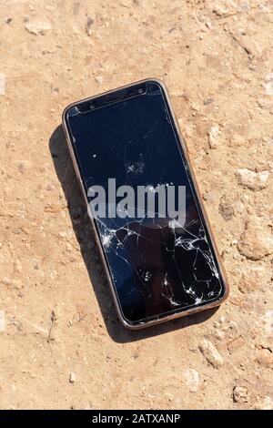 A cellular telephone on the ground, its dark screen shattered. Stock Photo