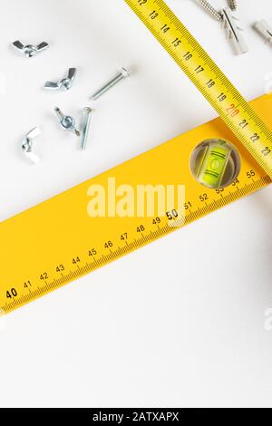 Yellow tape measure spirit level and wing nuts on clear white background. Vertical photo. Place for text. Stock Photo