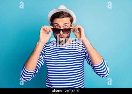 Photo of funky excited handsome guy tourist taking off cool black sun specs open mouth read discounts banner wear striped sailor shirt cap isolated Stock Photo