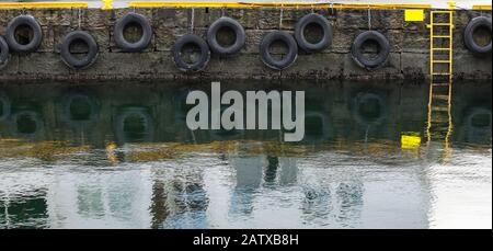 Grungy concrete mooring wall with hanging tires as bumpers, background photo texture Stock Photo