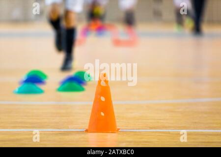 Indoor soccer futsal training field. Athletes training soccer indoor during winter time. Orange soccer cone and colorful markers on wooden floor Stock Photo