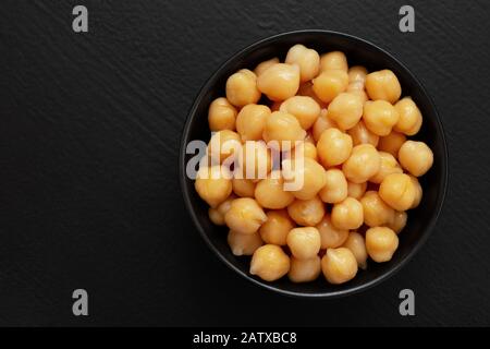 Cooked chick peas in a black ceramic bowl isolated on black painted wood. Top view. Stock Photo