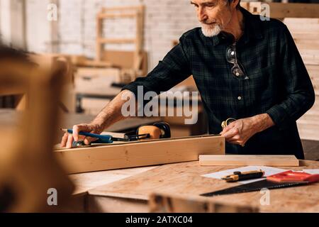 Carpenter measuring wooden plank with tape measure in workshop Stock Photo