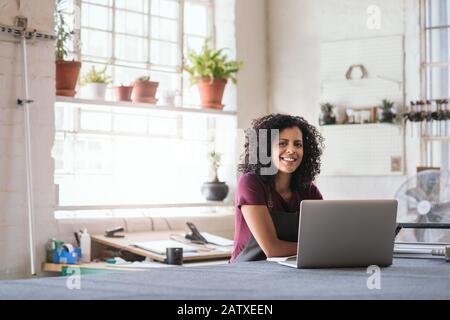 Smiling young woman using a laptop in her framing shop Stock Photo