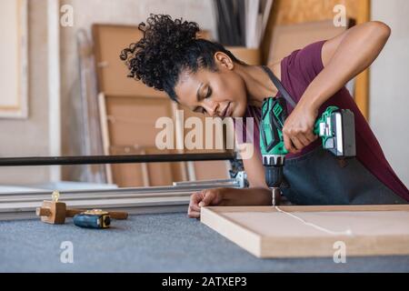 Woman assembling a frame with a drill in her workshop Stock Photo