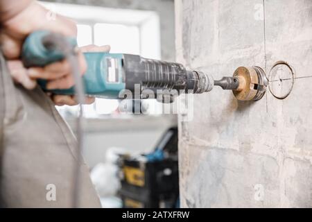 Boring hole in wall for electric outlet by power hammer drills tool Stock Photo