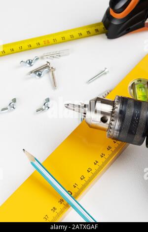 Yellow tape measure spirit level drill, pencil and wing nuts on clear white background. Vertical photo. Place for text. Stock Photo