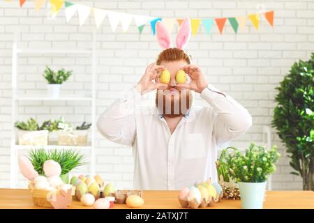 Happy easter.A funny fat man decorates eggs while sitting at a table with easter decor in the background Stock Photo