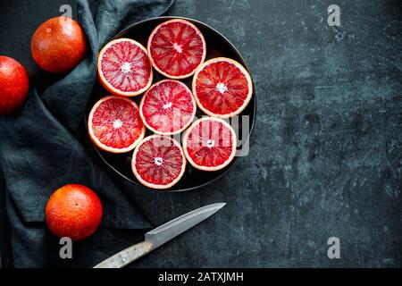 Cutted blood oranges in a plate on a dark black background. Top view, flat lay composition, copy space. Stock Photo