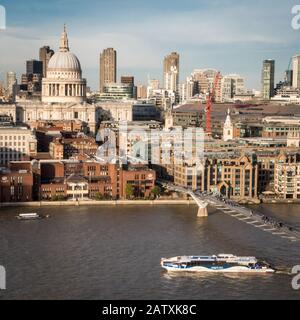 A river bus on the River Thames passing the Millennium Bridge and St. Paul's cathedral on the north bank. Stock Photo