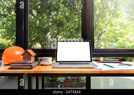 Laptop with helmet and architects house model on desk. Stock Photo