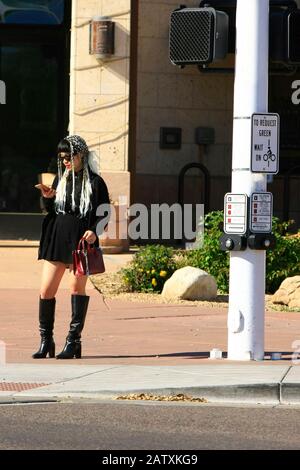 Trendy young woman using her cellphone whilst waiting at a crosswalk in downtown Old Town Scottsdale AZ Stock Photo