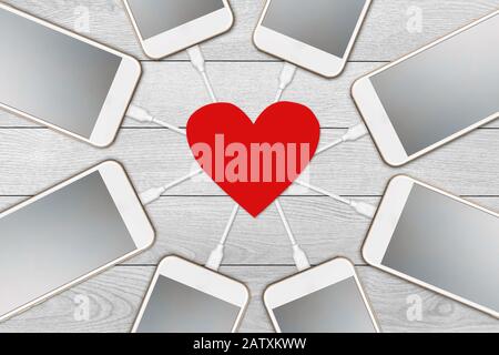 On white wooden background isolated  Several smart phones with a blank screen that is charging from the heart of red paper, the concept of the power o Stock Photo