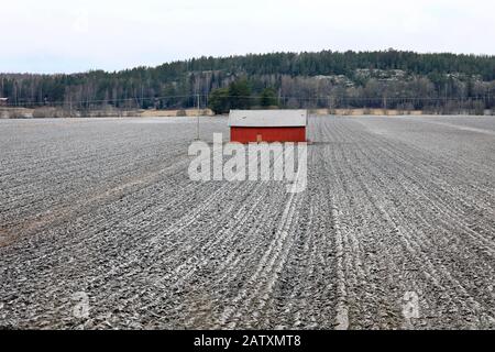 Red wooden barn in a lightly snow-covered field on an overcast day of winter. Sauvo, Finland. December 26, 2019. Stock Photo