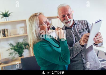 Senior couple singing karaoke at home, having fun. Stock Photo