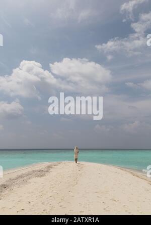 Concept Travel -Woman on beach; A lone woman standing on a tropical beach with white sand, blue sky and turquoise water, rear view,  the Maldives,Asia Stock Photo
