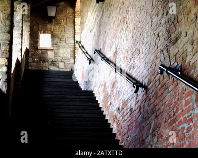 Concrete exterior stair in covered brick and stone castle wall with textured brick wall on one side and staggered old vintage black steel railing. Stock Photo