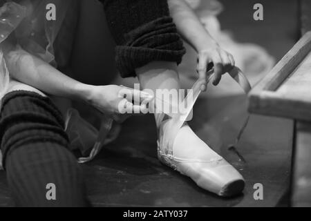 Ballerina sits on the floor in the theater's rehearsal hall and puts on pointe shoes Stock Photo