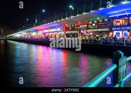 Tourists relax in the restaurants located on the first level of the famous Galata Bridge at night, Istanbul, Turkey Stock Photo