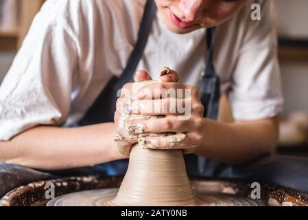 Potter working on a Potter's wheel making a vase. Young woman forming the clay with her hands creating jug in a workshop. Close up Stock Photo