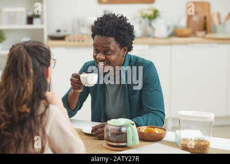 African happy man drinking coffee and smiling to his girlfriend during breakfast in the kitchen Stock Photo
