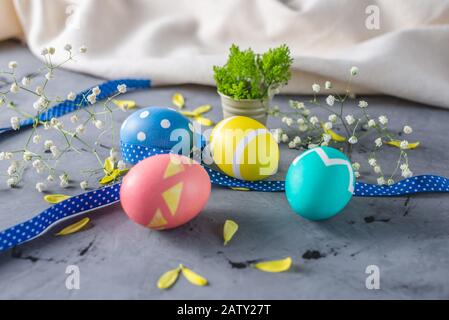 Bright colorful Easter eggs with a ribbon and spring flowers on a gray background. Festive spring Easter card. Stock Photo