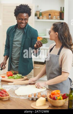 Young couple having fun in the kitchen during their cooking they preparing vegetable salad and making dough Stock Photo