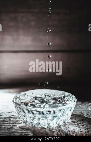 Water drops splashing into glass bowl of water Stock Photo