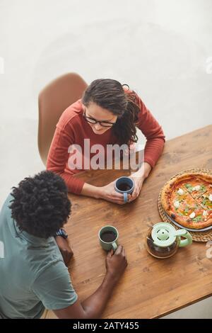High angle view of young couple sitting at wooden table talking and drinking coffee with pizza Stock Photo