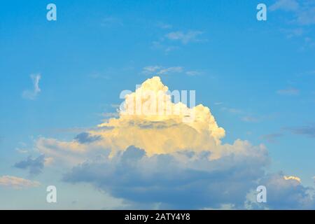 Single bright white dreamlike cloud on a blue dramatic sky. One cloud backlit by the sun Stock Photo