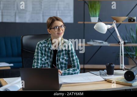 Female interior designer working in office with laptop. Architect thinks over architectural plan, searching new ideas for construction project. Woman Stock Photo