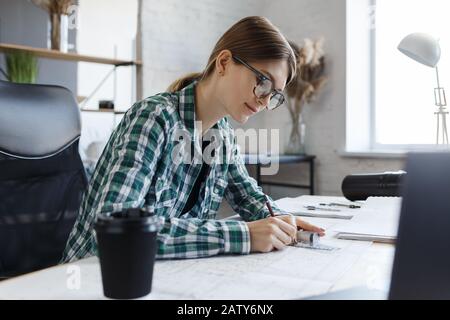 Architect drawing blueprints in office. Engineer sketching a construction project. Architectural plan. Close-up portrait of beautiful woman concentrat Stock Photo