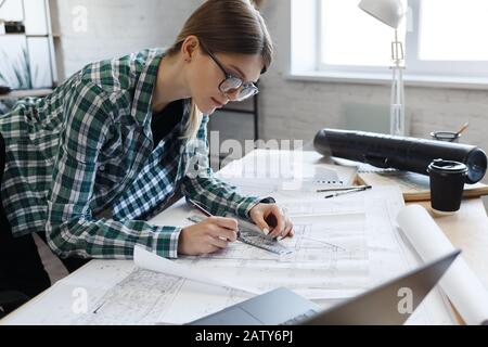 Architect drawing blueprints in office. Engineer sketching a construction project. Architectural plan. Close-up portrait of beautiful woman concentrat Stock Photo