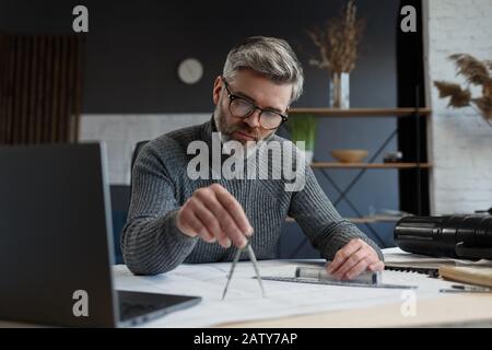 Interior designer working in office with blueprints.Engineer inspect architectural plan, sketching a construction project.Portrait of handsome bearded Stock Photo