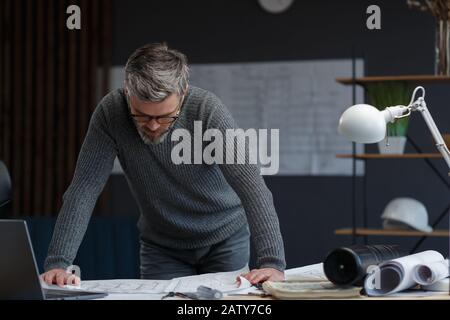Architect working in office with blueprints.Engineer inspect architectural plan, sketching a construction project.Portrait of handsome bearded man sit Stock Photo