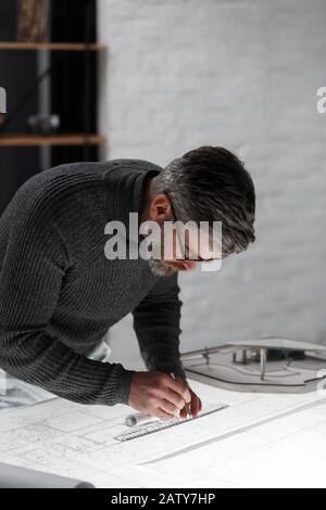 Architect drawing blueprints in office. Engineer sketching a construction project. Architectural plan. Close-up portrait of handsome bearded man conce Stock Photo