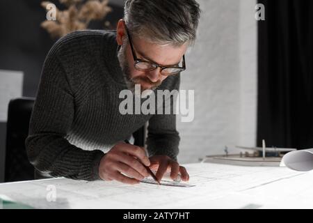 Architect drawing blueprints in office. Engineer sketching a construction project. Architectural plan. Close-up portrait of handsome bearded man conce Stock Photo